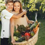 Mother and son smiling outdoors with a basket full of fresh vegetables, embracing in a sunny garden.