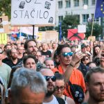 A large group of people peacefully protesting in Bratislava, Slovakia with signs and flags.